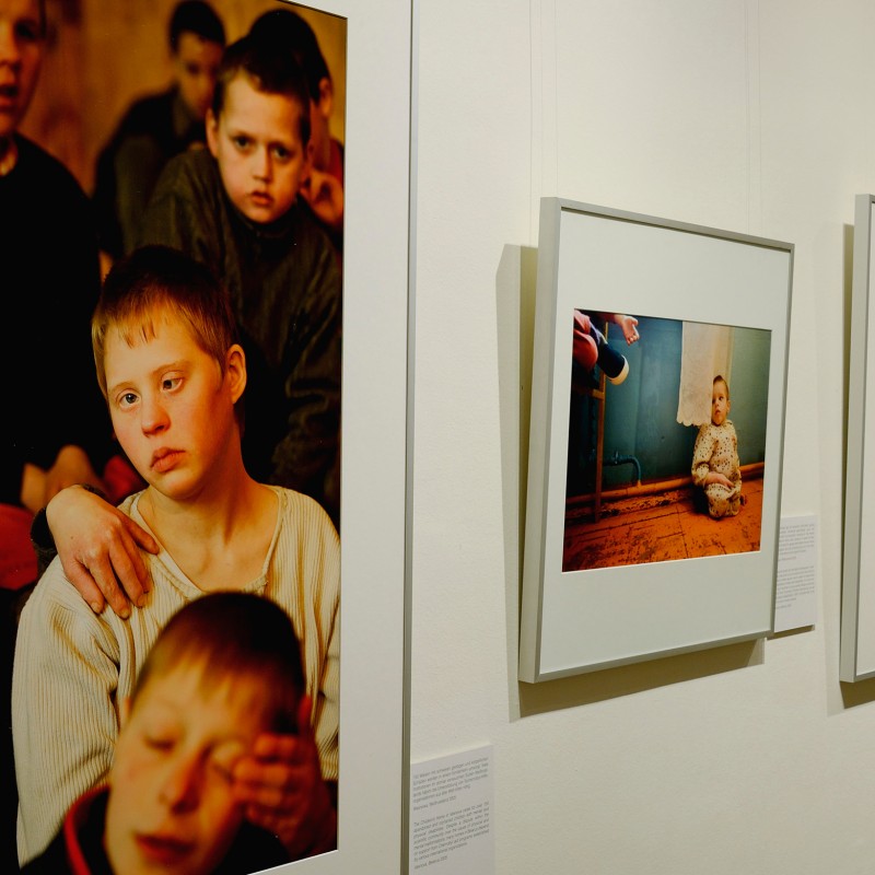 Photographs displayed in an exhibition, including a large portrait of several children and two smaller framed photos
                                 of children in indoor settings. (AI-generated alt-text, generated with GPT-4.1-mini)