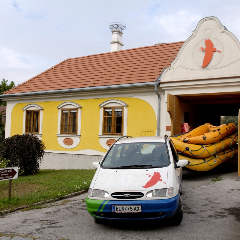 Yellow building with painted figure above the barn door, van with the same figure in front. Several yellow inflatable
                                 boats inside doorway. (AI-generated alt-text, generated with GPT-4.1-mini)