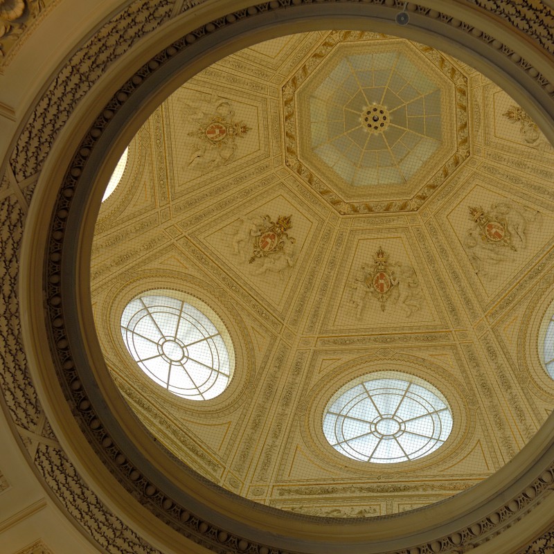 Ornate dome with intricate stucco patterns, round windows, and octagonal skylight, viewed from below. (AI-generated
                                 alt-text, generated with GPT-4.1-mini)