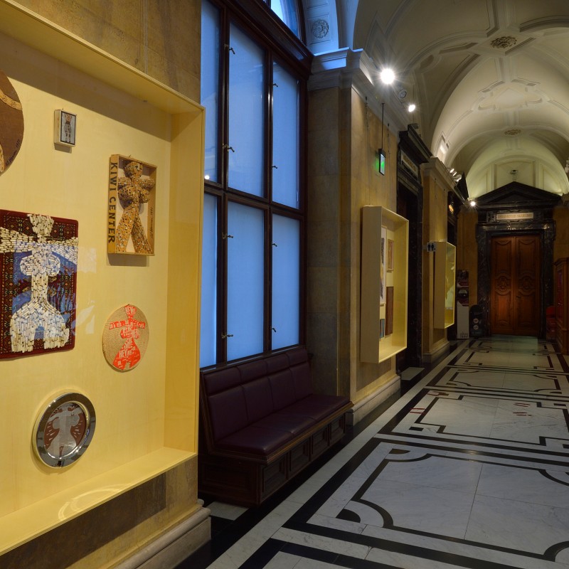 Display case with several colorful collages beside a long hallway with a high vaulted ceiling and geometric patterned
                                 floor. (AI-generated alt-text, generated with GPT-4.1-mini)