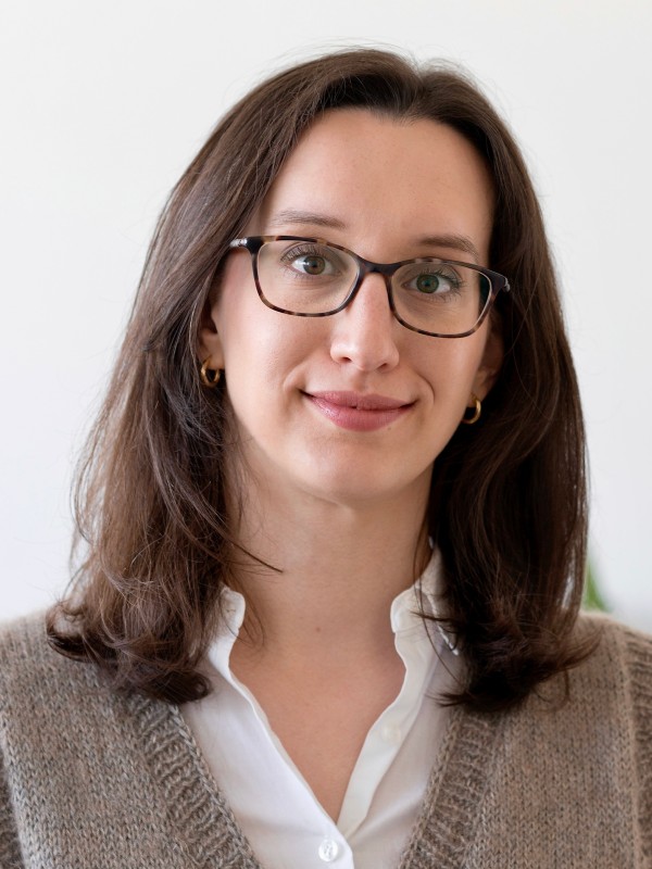 Frau mit schulterlangem
                                 braunem Haar und Brille vor hellem Hintergrund, trägt weiße Bluse und braunen Pullover, lächelt leicht. (KI-generierter Alt-Text,
                                 erstellt mit GPT-4.1-mini)