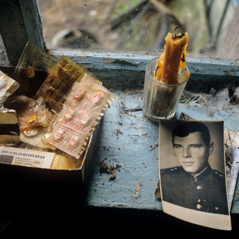 Old portrait photo of a man in uniform beside a burnt candle, multiple medicine blister packs, and small everyday
                                 items on a windowsill. (AI-generated alt-text, generated with GPT-4.1-mini)