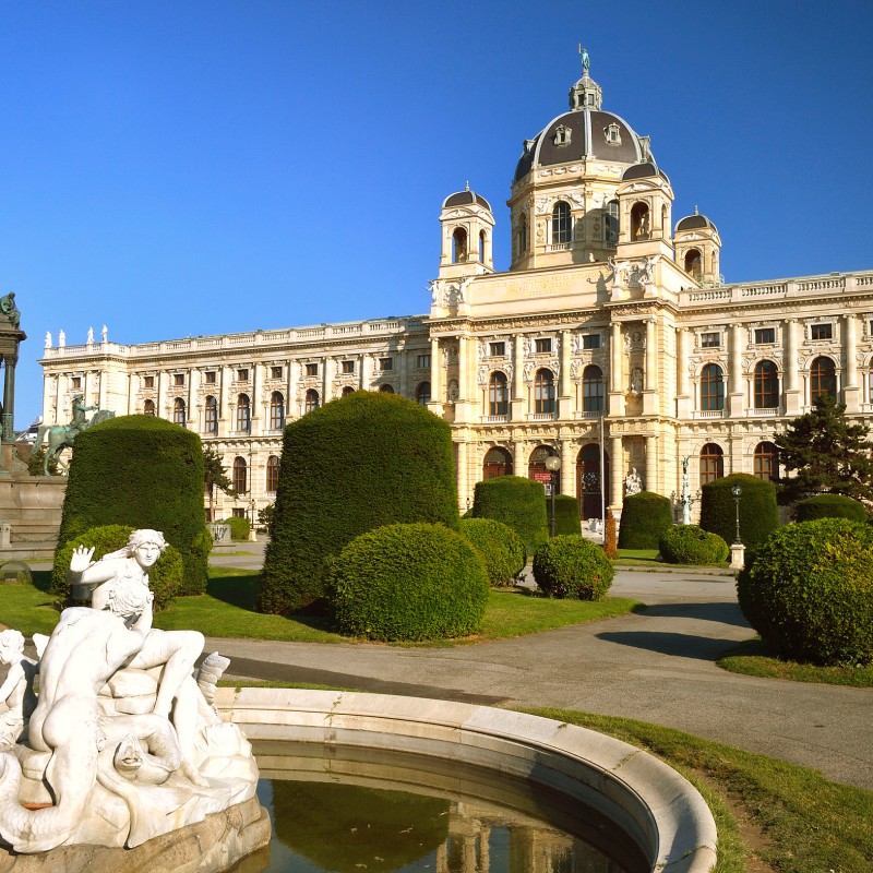 View of the facade of the Natural History Museum Vienna with manicured garden, hedges, fountain, and several statues
                                 in the foreground. (AI-generated alt-text, generated with GPT-4.1-mini)