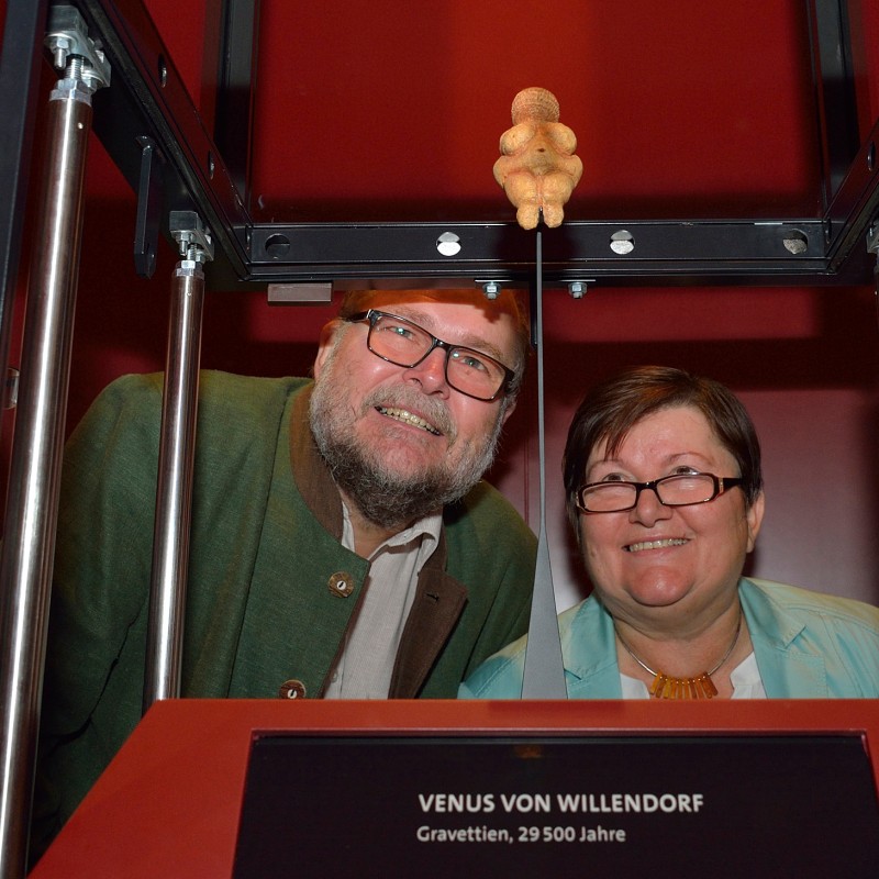 Four
                                 people smiling and looking through a display case at the small Venus von Willendorf figure suspended above. (AI-generated
                                 alt-text, generated with GPT-4.1-mini)