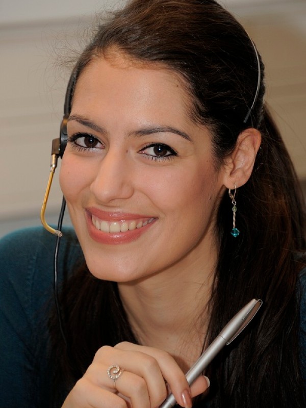 Junge Frau mit Headset, dunklen Haaren und dezenter Ohrhängern, hält einen Stift in der Hand und lächelt freundlich.
                                 (KI-generierter Alt-Text, erstellt mit GPT-4.1-mini)
