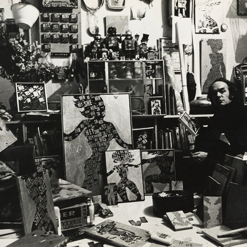 Black-and-white shot of a man surrounded by paintings, sculptures, and art supplies in a studio. A hairless mannequin
                                 stands on the right. (AI-generated alt-text, generated with GPT-4.1-mini)