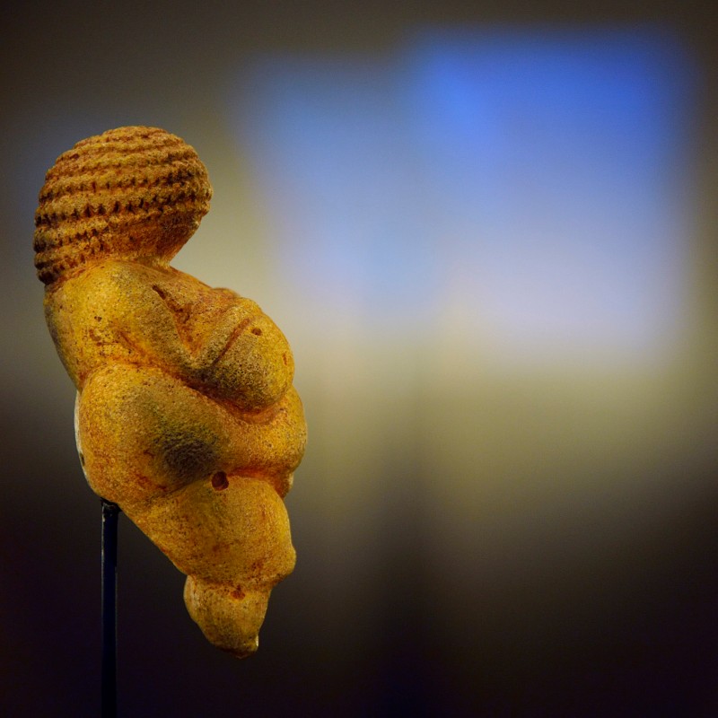 Venus of Willendorf, prehistoric female figurine with rounded
                                 body, side-lit against a dark background. (AI-generated alt-text, generated with GPT-4.1-mini)