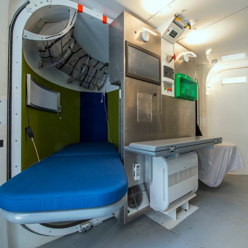 Sleeping cabin with blue mattress, recessed wall area, and technical equipment mounted on the wall. (AI-generated
                                 alt-text, generated with GPT-4.1-mini)