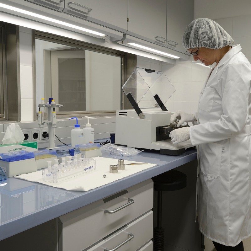 Person in a white lab coat and hairnet operates an analyzer at a shiny lab bench with lab equipment and test tubes.
                                 (AI-generated alt-text, generated with GPT-4.1-mini)