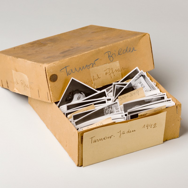 Open cardboard box containing multiple black-and-white photographs, some photos sticking out. Handwritten notes
                                 on the box. (AI-generated alt-text, generated with GPT-4.1-mini)