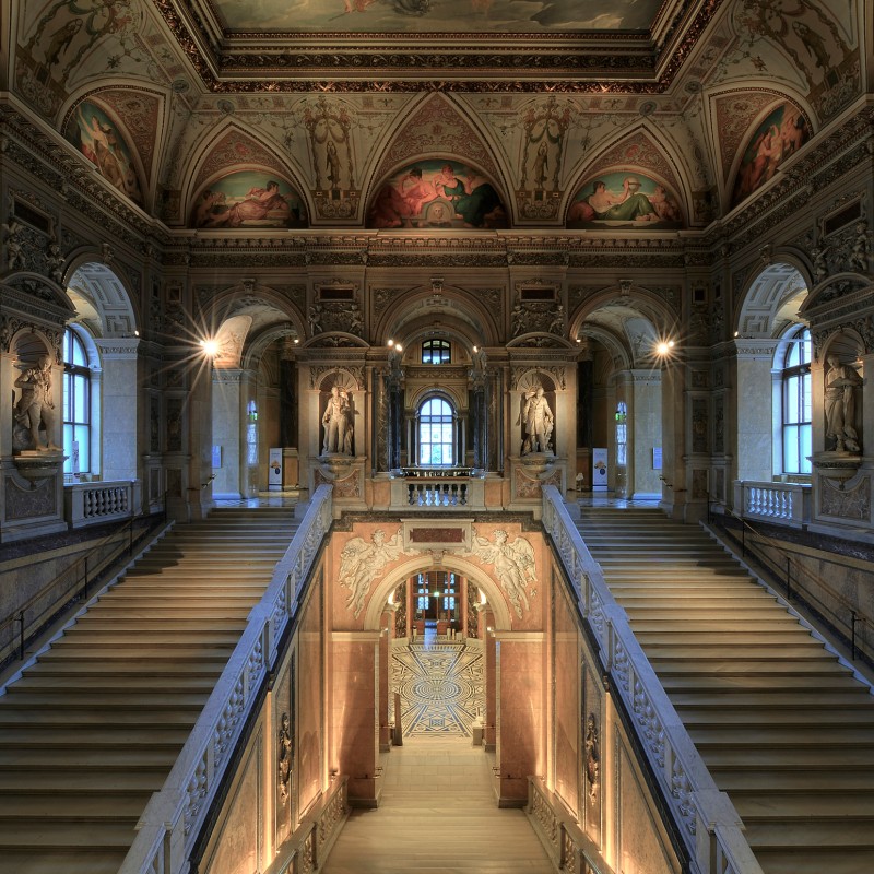 Monumentales Stiegenhaus mit prunkvollen Deckenfresken, marmorne Stufen, beidseitigen Balustraden und klassischen
                                 Statuen. (KI-generierter Alt-Text, erstellt mit GPT-4.1-mini)
