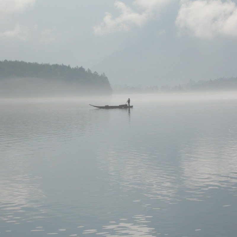 Boot mit einer Person auf einem See im Nebel