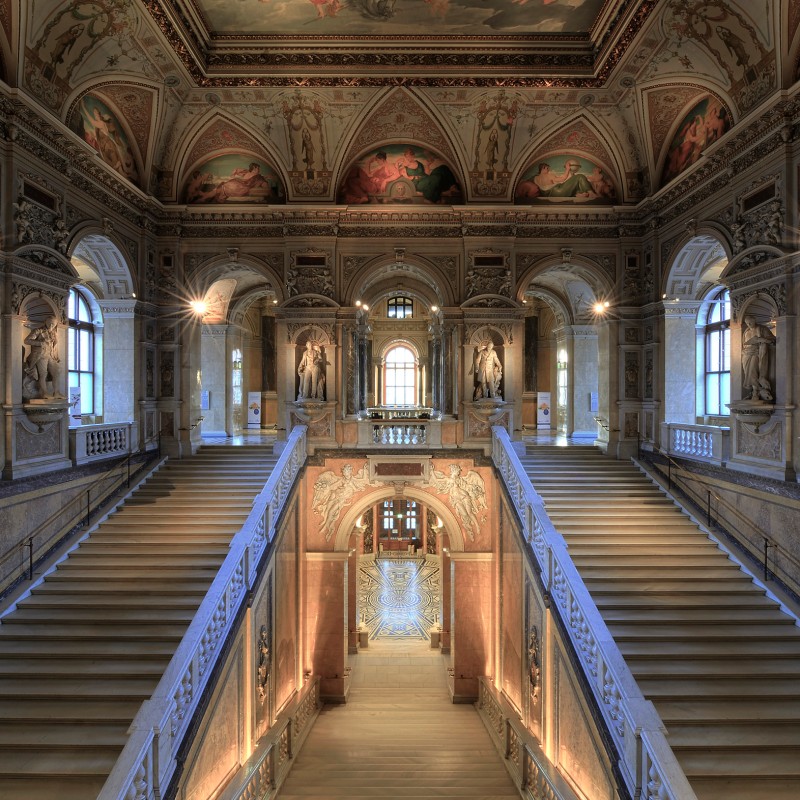 Prächtiges Stiegenhaus mit breiter Doppeltreppe, prunkvoll bemaltem Deckengewölbe und reich verzierten Balustraden.
                                 (KI-generierter Alt-Text, erstellt mit GPT-4.1-mini)