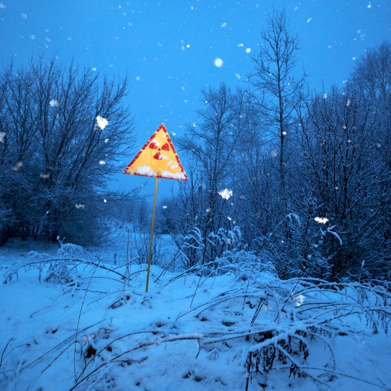 Bright yellow warning sign with radiation symbol on a pole in a snowy winter landscape, bare trees in the background.
                                 (AI-generated alt-text, generated with GPT-4.1-mini)