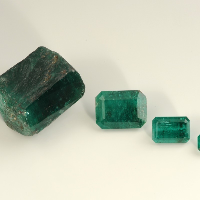 Uncut emerald and three cut emeralds from Habachtal side by side on a light surface. (AI-generated alt-text, generated
                                 with GPT-4.1-mini)