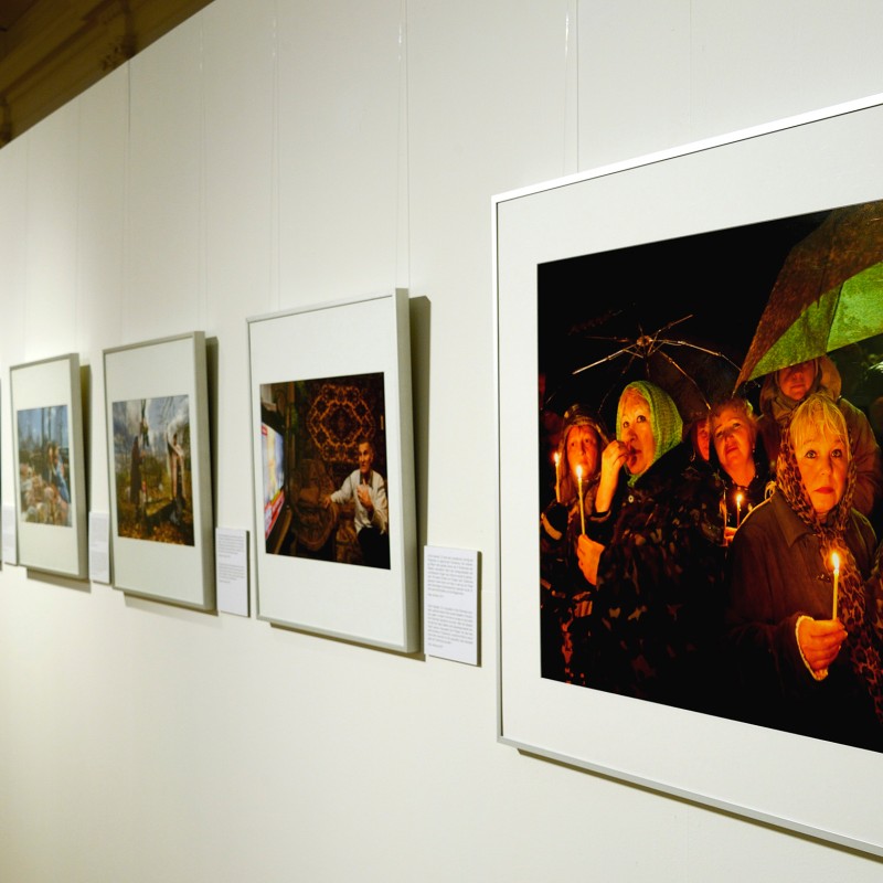 Photographs are arranged in a row on a white exhibition wall. In front, a large color photograph shows people holding
                                 lit candles and umbrellas. (AI-generated alt-text, generated with GPT-4.1-mini)