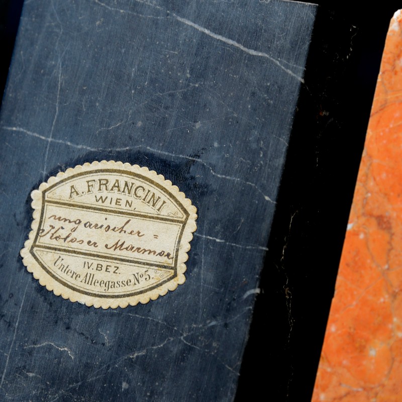 Dark blue-black marble slab with label reading 'A. Francini Wien ungarischer Koloser Marmor IV. BEZ Untere Allegasse
                                 No 5' next to part of an orange marble slab (AI-generated alt-text, generated with GPT-4.1-mini)
