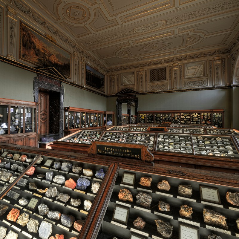 : Exhibition room with multiple display cases containing rocks and minerals, ornate ceiling, large windows, and wall paintings. (AI-generated alt-text, generated with GPT-4.1-mini)