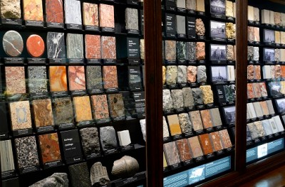 : Various large samples of building and decorative stones arranged in several rows in an illuminated display case, each with small labels. (AI-generated alt-text, generated with GPT-4.1-mini)