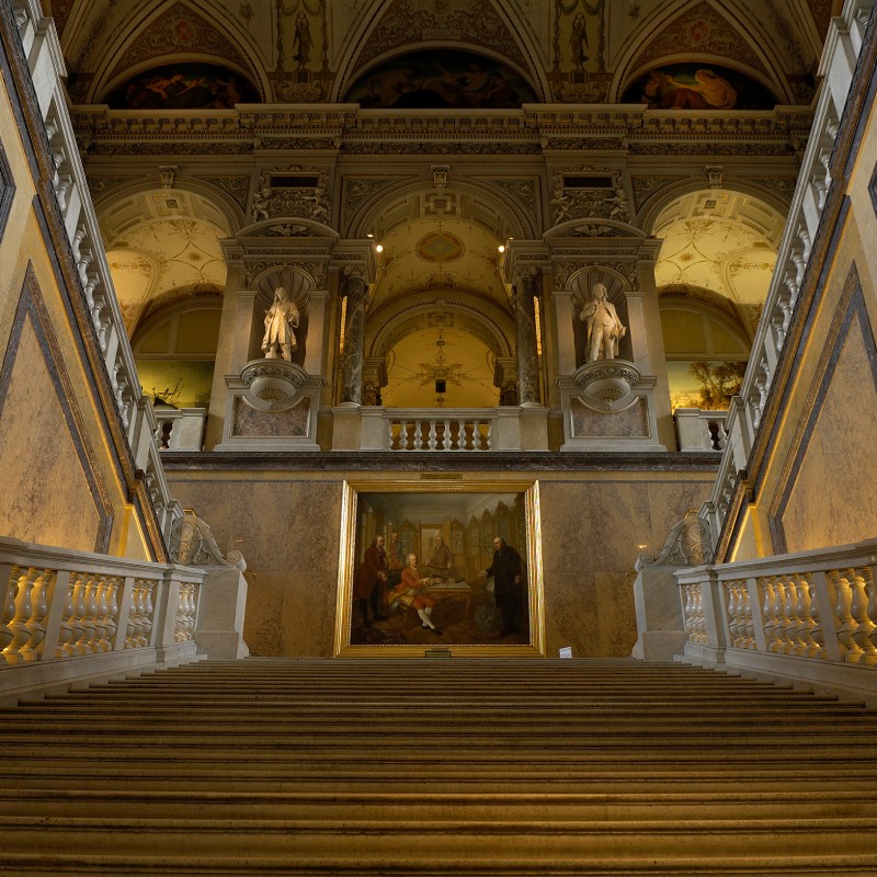 Ornate stone staircase with decorated railings, wall paintings, and statues inside a historic building. (AI-generated
                                 alt-text, generated with GPT-4.1-mini)