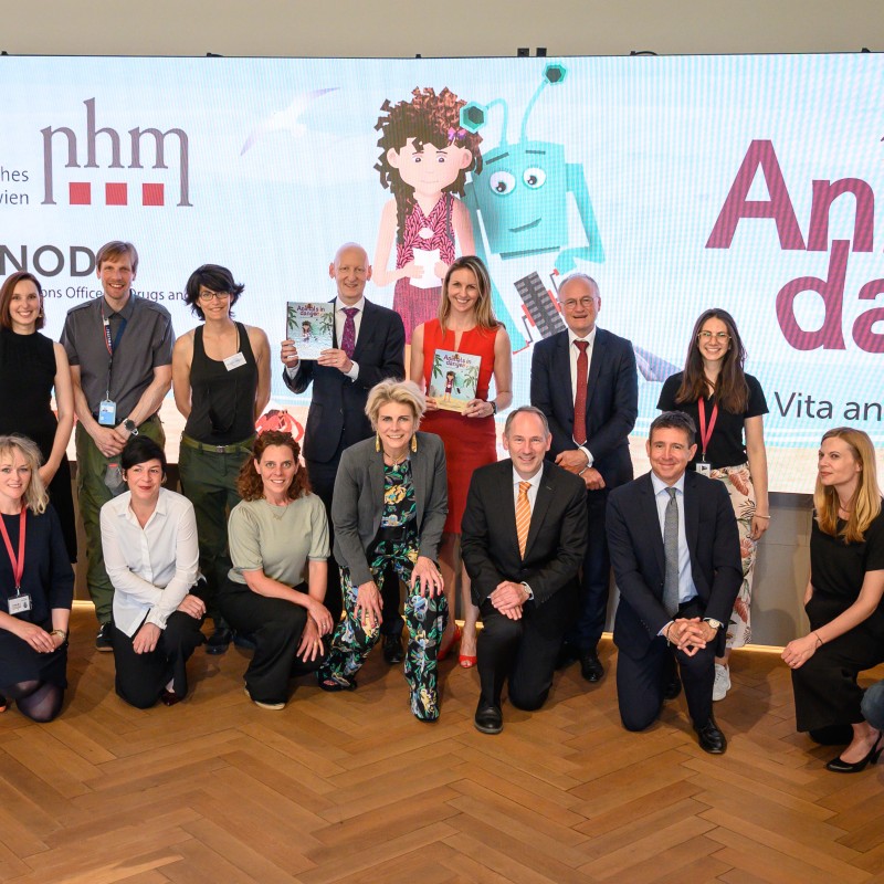 Gruppe von sechzehn Personen posiert lächelnd in zwei Reihen vor Bühnenbild mit den Logos des Naturhistorischen
                                 Museums Wien und UNODC sowie Aufschrift 'Animals in danger'. Drei Personen in der Mitte halten Bücher. (KI-generierter Alt-Text,
                                 erstellt mit GPT-4.1-mini)