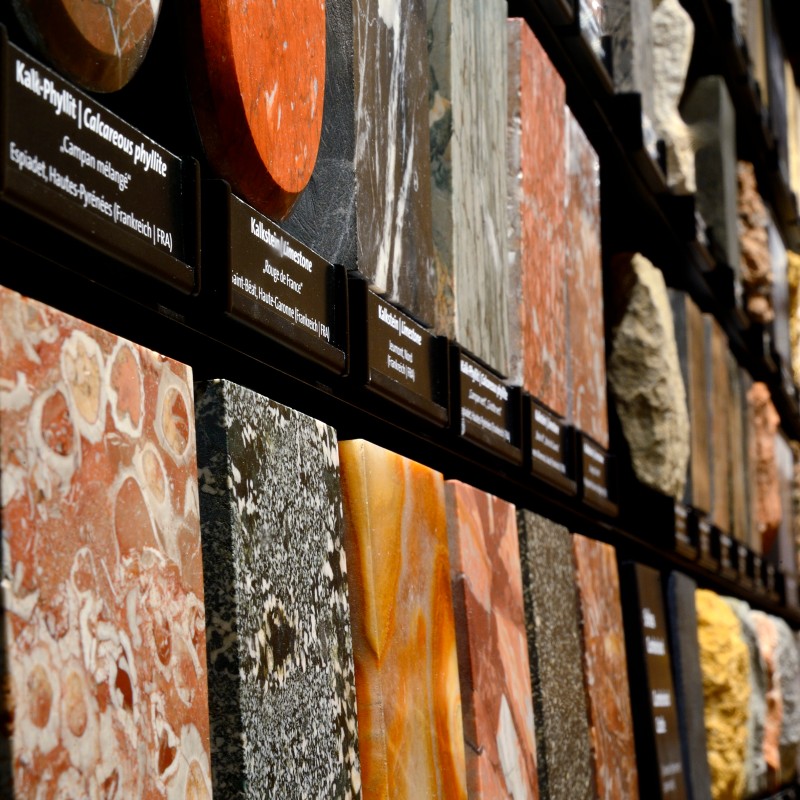 Rectangular rock specimens with various colors and patterns displayed side by side and stacked on a wall. (AI-generated
                                 alt-text, generated with GPT-4.1-mini)