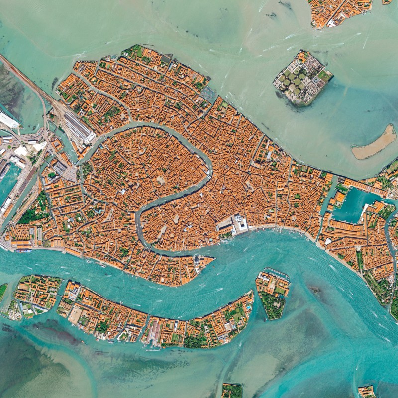 Aerial view of Venice showing dense historic buildings and canals, surrounded by turquoise water. (AI-generated
                                 alt-text, generated with GPT-4.1-mini)