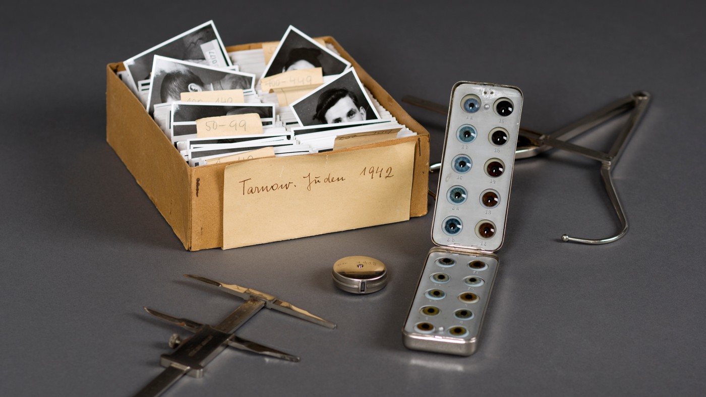 Brown box with black-and-white
                                 portrait photos, metal box with multiple glass objects, caliper, compass, small tin, and another metal instrument on a gray
                                 surface. (AI-generated alt-text, generated with GPT-4.1-mini)