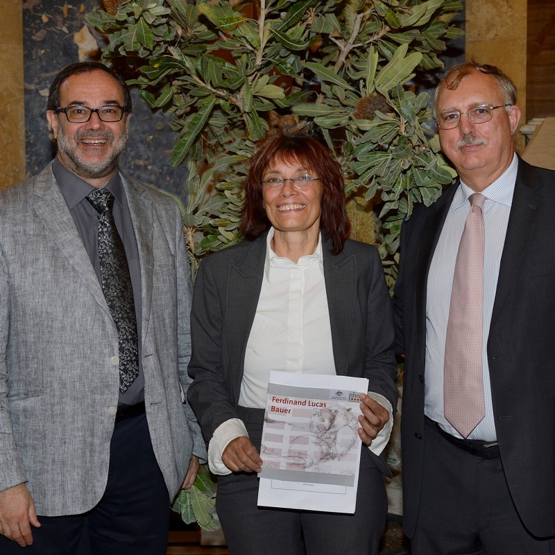 Drei Personen im Anzug und Kostüm stehen nebeneinander und lächeln, eine Frau in der Mitte hält ein Magazin mit
                                 dem Titel 'Ferdinand Lucas Bauer'. Im Hintergrund eine große Pflanze und eine Treppe. (KI-generierter Alt-Text, erstellt mit
                                 GPT-4.1-mini)