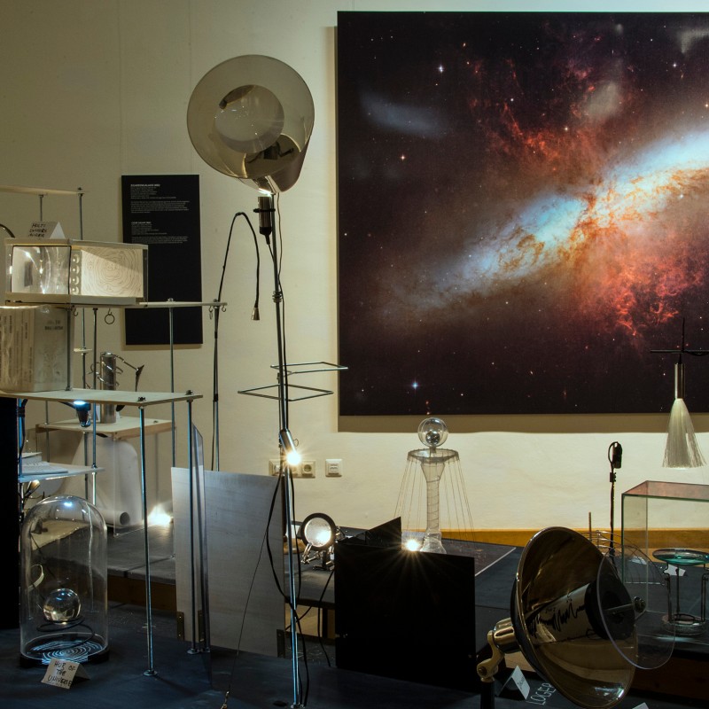 Art
                                 installation with glass and metal objects on pedestals, large space image with galaxy in the background. (AI-generated alt-text,
                                 generated with GPT-4.1-mini)