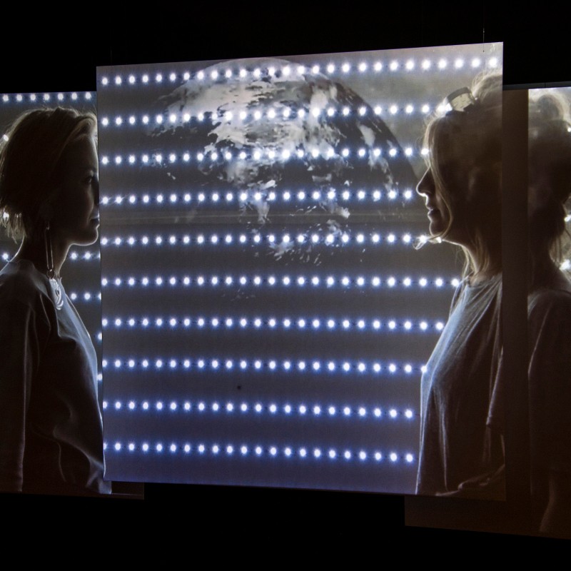 Two
                                 women in profile facing each other against a wall illuminated with horizontal light dots and a world map. (AI-generated alt-text,
                                 generated with GPT-4.1-mini)