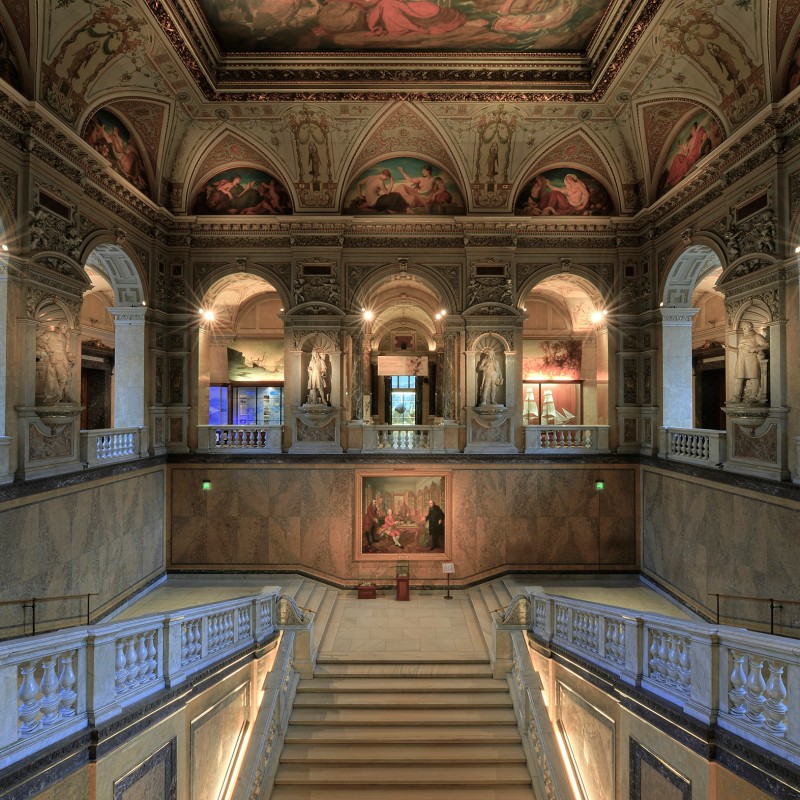 Prächtiges Treppenhaus mit kunstvollen Fresken an Decke und Wänden, Skulpturen in Nischen, Balustraden und zentralem
                                 Gemälde. (KI-generierter Alt-Text, erstellt mit GPT-4.1-mini)