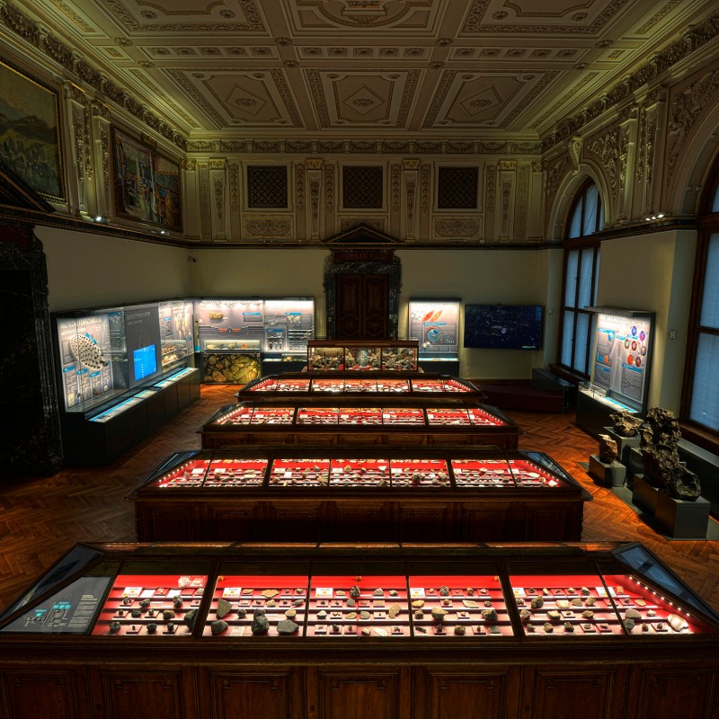 Ornately decorated historic exhibition hall with display cases filled with meteorites and explanatory panels at
                                 the Natural History Museum Vienna. (AI-generated alt-text, generated with GPT-4.1-mini)