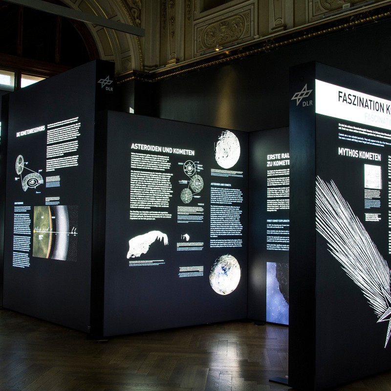 Schwarz-weiße
                                 Ausstellungstafeln mit Texten und Illustrationen über Kometen in einem Museumssaal mit hoher Decke. (KI-generierter Alt-Text,
                                 erstellt mit GPT-4.1-mini)