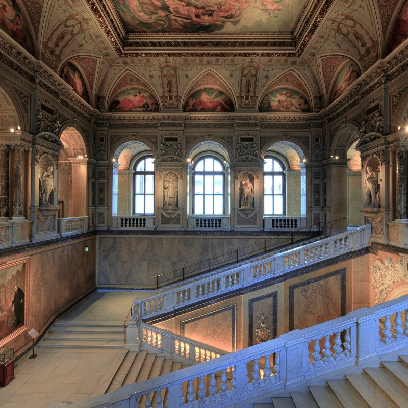 Ornate historic staircase with decorated vaulted ceilings, wide marble stairs, arched windows, and wall paintings.
                                 (AI-generated alt-text, generated with GPT-4.1-mini)