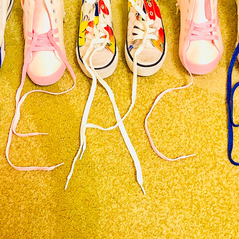 Three pairs of sneakers lined up, their shoelaces spelling out the word 'PEACE' on a yellow carpet. (AI-generated
                                 alt-text, generated with GPT-4.1-mini)