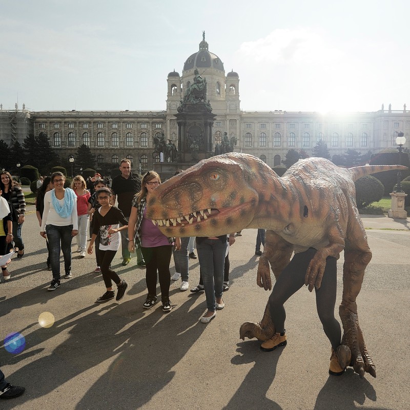 Life-sized dinosaur model outside the Natural History Museum Vienna, surrounded by a group of people. (AI-generated
                                 alt-text, generated with GPT-4.1-mini)