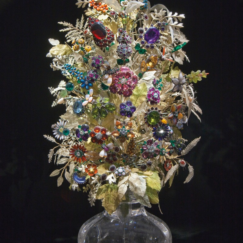 Colorful gemstone bouquet with various jewels set in gold-toned leaves, displayed in a clear glass vase (AI-generated
                                 alt-text, generated with GPT-4.1-mini)