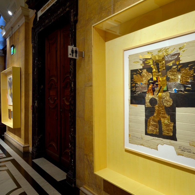 Artwork featuring gold and black elements behind glass in a lit museum corridor with other display cases and a decorative
                                 floor. (AI-generated alt-text, generated with GPT-4.1-mini)