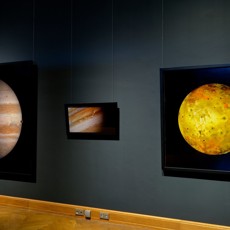 Three backlit depictions of celestial bodies side by side on a dark blue wall, wooden floor below. (AI-generated
                                 alt-text, generated with GPT-4.1-mini)