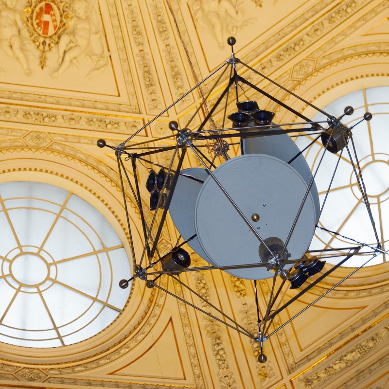 Large geometric structure made of metal rods and circular elements suspended from an ornate ceiling with two domed
                                 windows. (AI-generated alt-text, generated with GPT-4.1-mini)