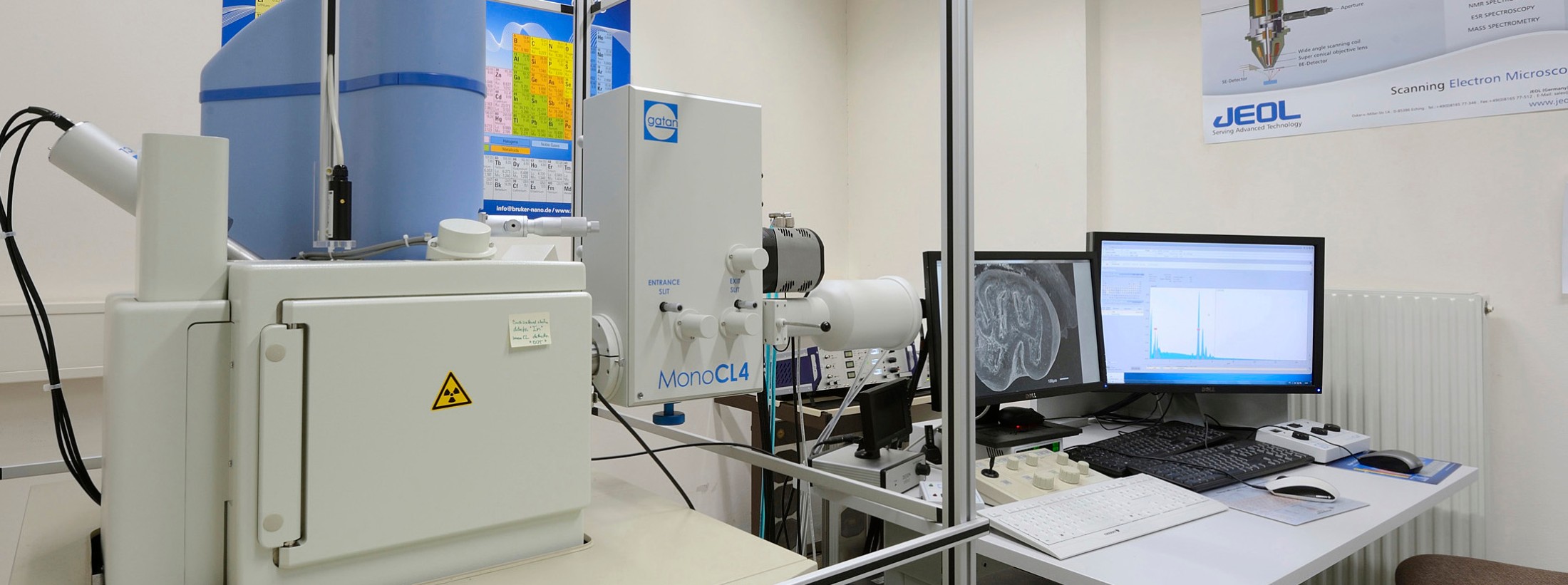 : Elektronenmikroskop mit mehreren Bildschirmen und Tastatur auf einem Labortisch, links Warnsymbol. (KI-generierter Alt-Text, erstellt mit GPT-4.1-mini)