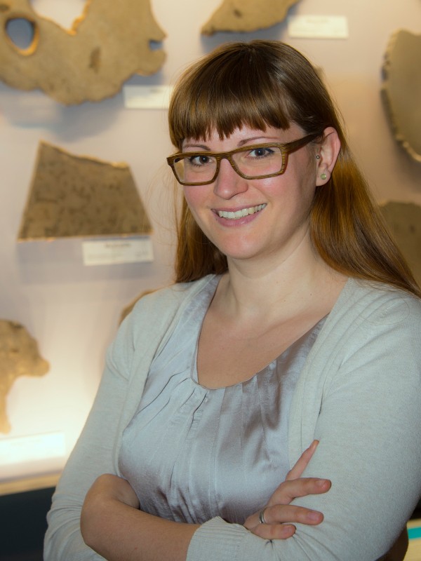 Junge Frau mit langen, glatten Haaren und Brille steht lächelnd mit verschränkten Armen vor einer Wand mit Mineralplatten.
                                 (KI-generierter Alt-Text, erstellt mit GPT-4.1-mini)