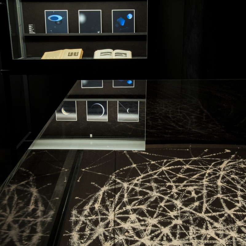 Glass display case with several photographs of moon phases, an open book, and graphics with white lines on a dark
                                 background. (AI-generated alt-text, generated with GPT-4.1-mini)