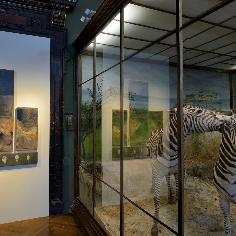 Zebras inside a museum glass case with a triptych painting and ornate black frame on the adjacent wall. (AI-generated
                                 alt-text, generated with GPT-4.1-mini)