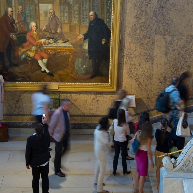 Crowd of people on a marble staircase in the entrance hall, statue of a woman in light clothing to the left of a
                                 large wall painting showing several men. (AI-generated alt-text, generated with GPT-4.1-mini)