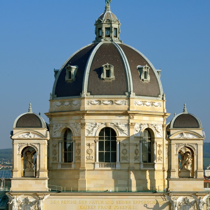 Central dome of the Natural History Museum with a statue on top and clearly visible reliefs on the facade. (AI-generated
                                 alt-text, generated with GPT-4.1-mini)