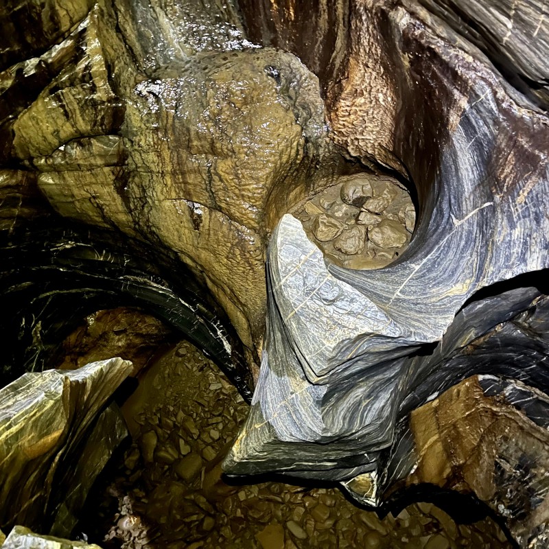 Gesteinsformation mit markanten Strudellöchern und rund geschliffenen Steinen in einer Höhle. (KI-generierter Alt-Text,
                                 erstellt mit GPT-4.1-mini)
