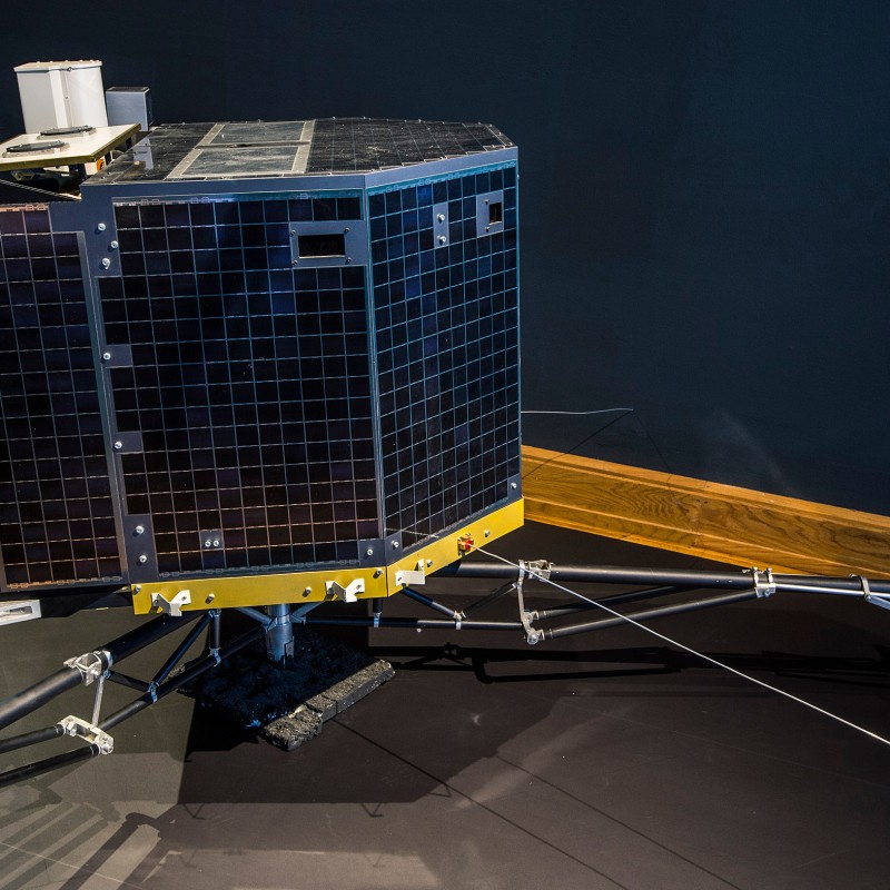 Sondensonde
                                 Philae mit schwarzer Verkleidung und mehreren ausladenden Beinen auf einer Präsentationsfläche. (KI-generierter Alt-Text,
                                 erstellt mit GPT-4.1-mini)